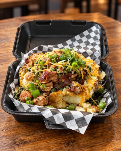 Overflowing baked potato with steak, chicken, bacon, shredded cheese and green onions